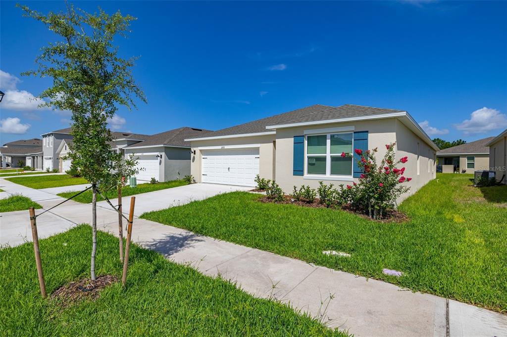 A single-story suburban house with a two-car garage, blue shutters, and a landscaped front yard — 2893 HOUSE FINCH ROAD, HARMONY, FL
