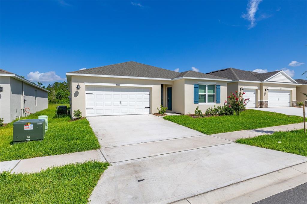 A single-story suburban house with a white garage, beige stucco siding, and blue shutters — 2893 HOUSE FINCH ROAD, HARMONY, FL