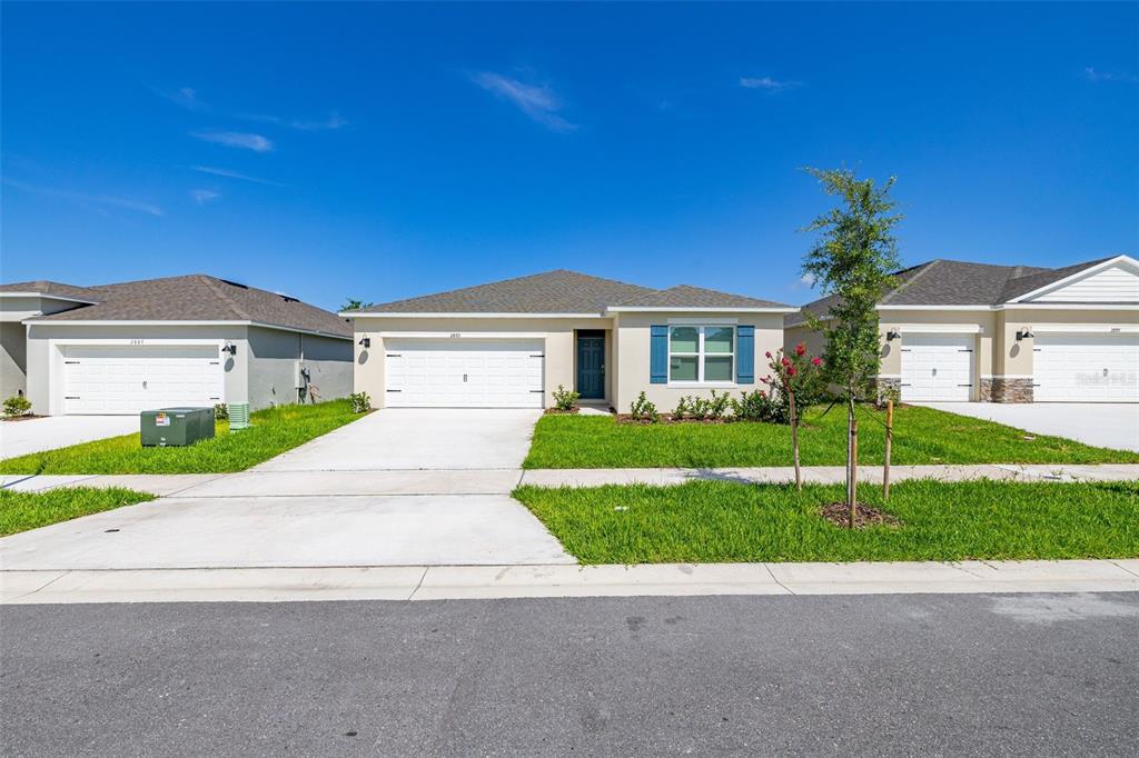 A single-story suburban house with a two-car garage, light stucco exterior, and blue shutters — 2893 HOUSE FINCH ROAD, HARMONY, FL