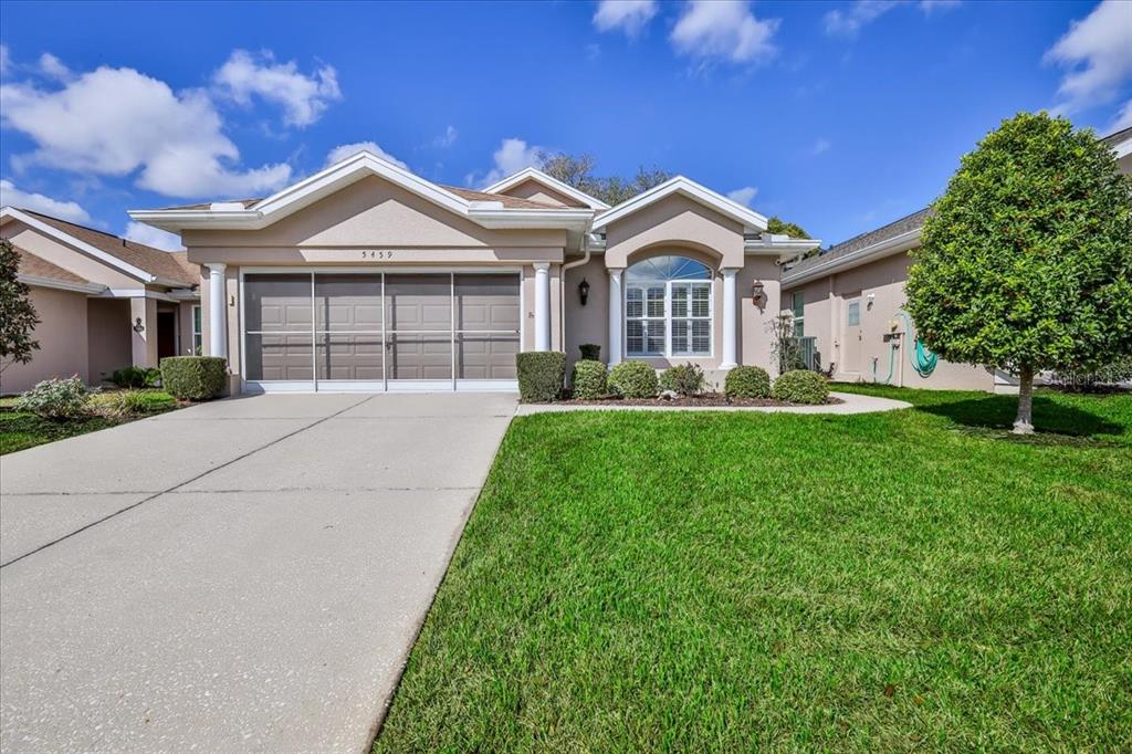 A single-story house with a beige stucco exterior, a two-car garage, and a front lawn — 5459 LEGEND HILLS LANE, SPRING HILL, FL