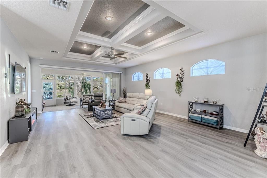 A living room features a coffered ceiling, light wood-look flooring, and sliding glass doors — 5459 LEGEND HILLS LANE, SPRING HILL, FL