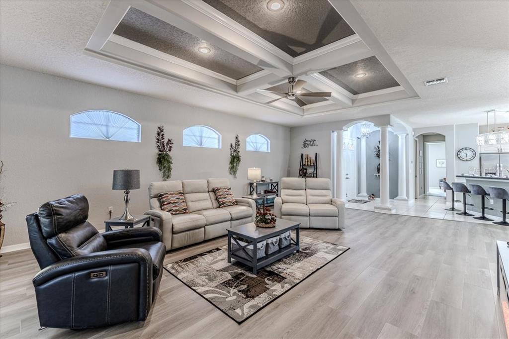 A living room features a tray ceiling, light wood flooring, and a neutral seating area — 5459 LEGEND HILLS LANE, SPRING HILL, FL