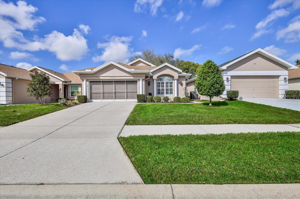 A single-story suburban house with a tan exterior, a two-car garage, and a front lawn — 5459 LEGEND HILLS LANE, SPRING HILL, FL