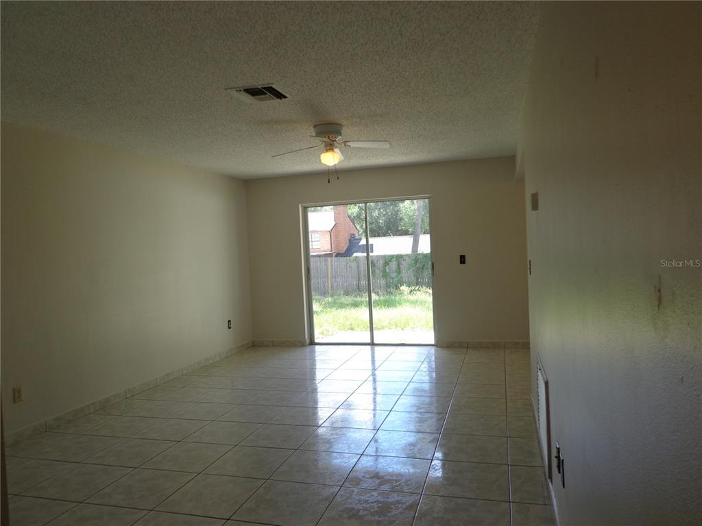 A living room with light-colored tile flooring, a ceiling fan, and sliding glass patio doors — 721 REGENT CIRCLE S, BRANDON, FL