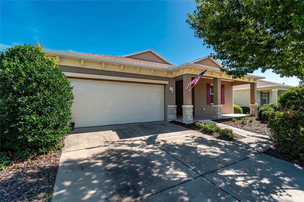 A single-story house with a two-car garage, stone-accented porch, and an American flag — 7847 SW 82ND PLACE, OCALA, FL
