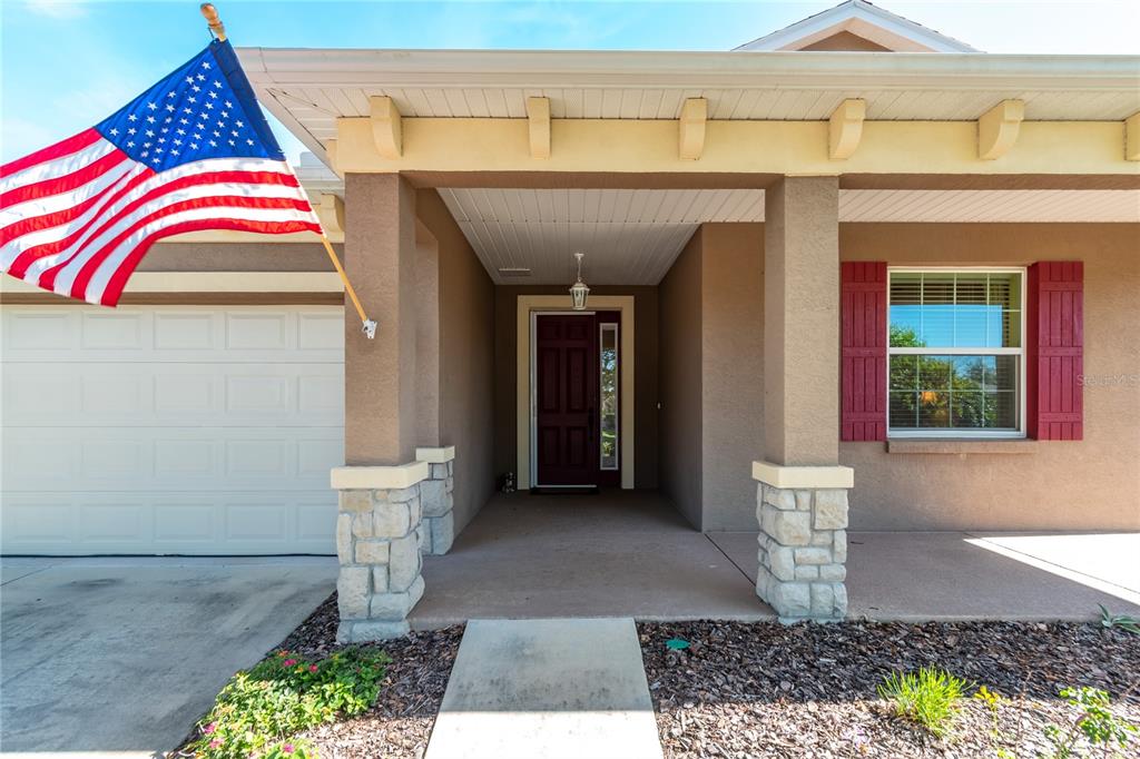 The exterior of a house features a covered porch, stone pillars, and an American flag — 7847 SW 82ND PLACE, OCALA, FL