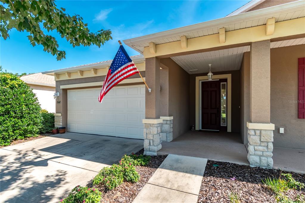 A single-story house exterior features a two-car garage, a covered entryway, and an American flag — 7847 SW 82ND PLACE, OCALA, FL