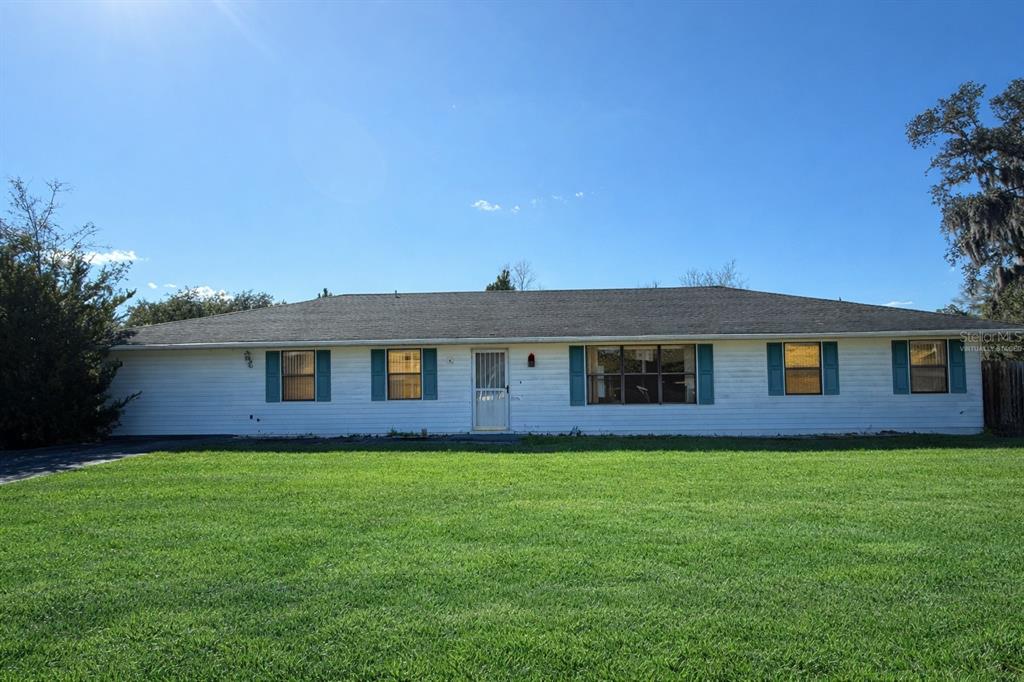 A single-story white house with blue shutters sits behind a large green lawn — 34847 LEARN ROAD, LEESBURG, FL