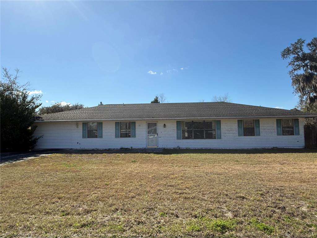A single-story white house with a gray shingled roof and blue shutters sits on a lawn — 34847 LEARN ROAD, LEESBURG, FL