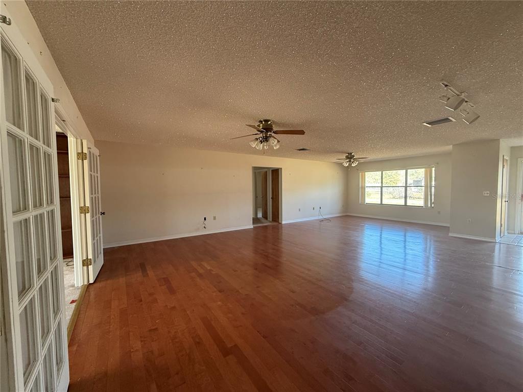 A large, empty living room features hardwood floors, two ceiling fans, and a popcorn ceiling — 34847 LEARN ROAD, LEESBURG, FL