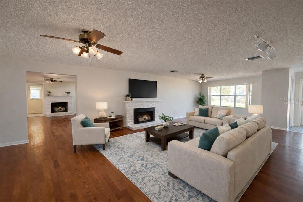 A spacious living room features a white brick fireplace, hardwood floors, and two ceiling fans — 34847 LEARN ROAD, LEESBURG, FL