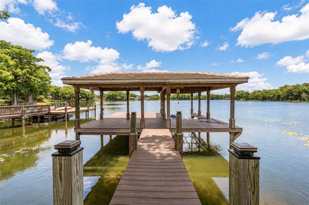 A wooden boat dock with a covered slip extends into a calm lake under clouds — 2914 REEF KNOT PLACE, WINTER PARK, FL