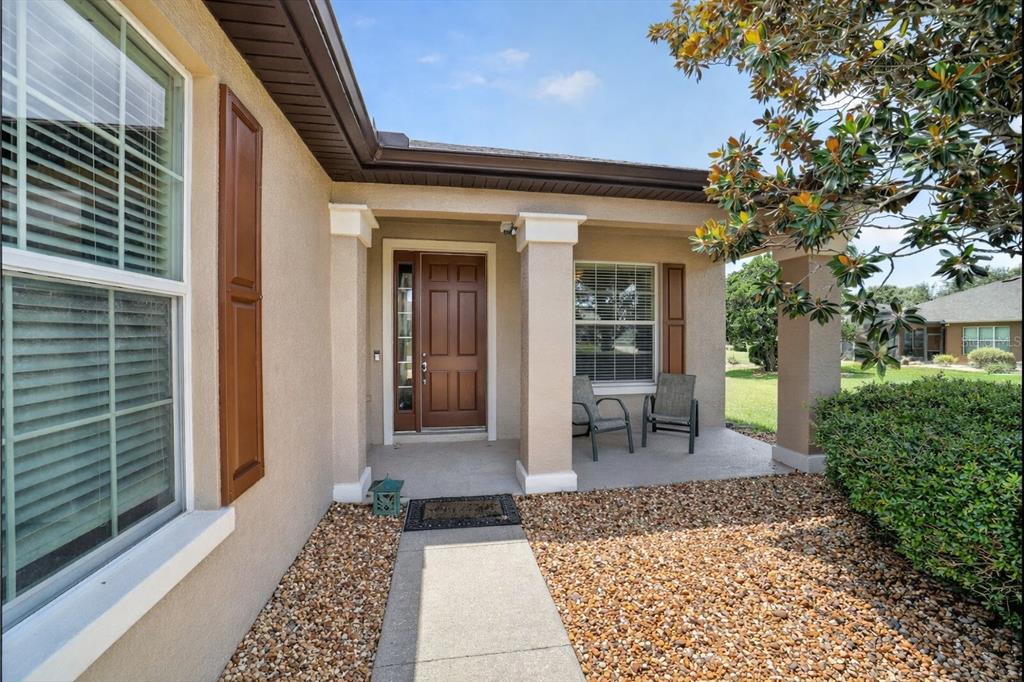 A tan house exterior features a covered front porch, brown door, and gravel landscaping — 9824 SW 72ND LANE, OCALA, FL