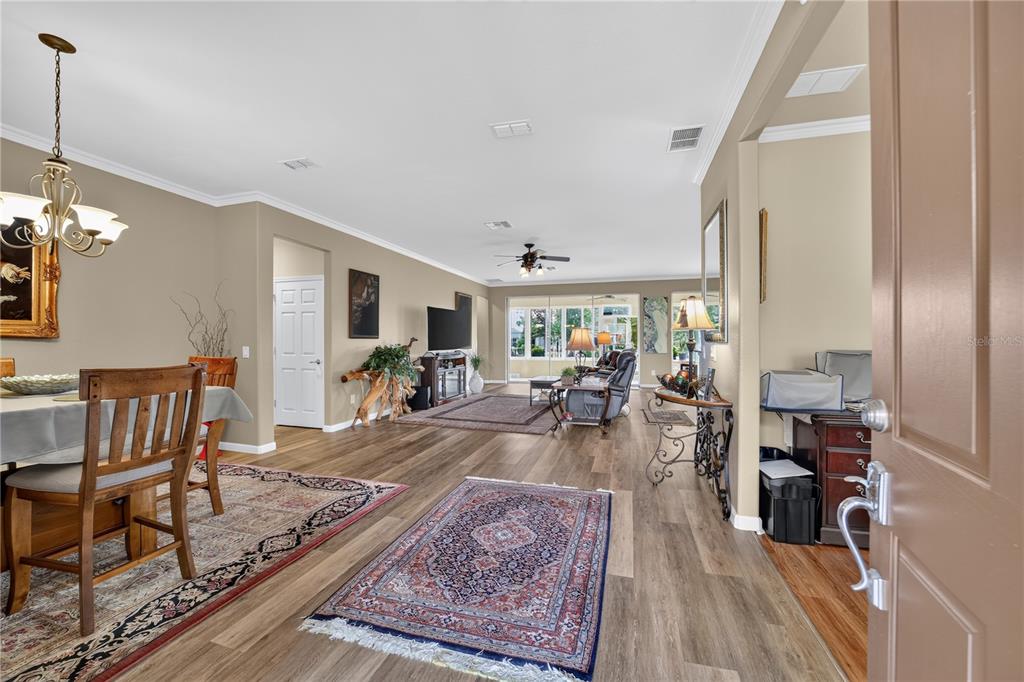 An open-concept living and dining area features wood-look flooring, area rugs, and a ceiling fan — 9824 SW 72ND LANE, OCALA, FL