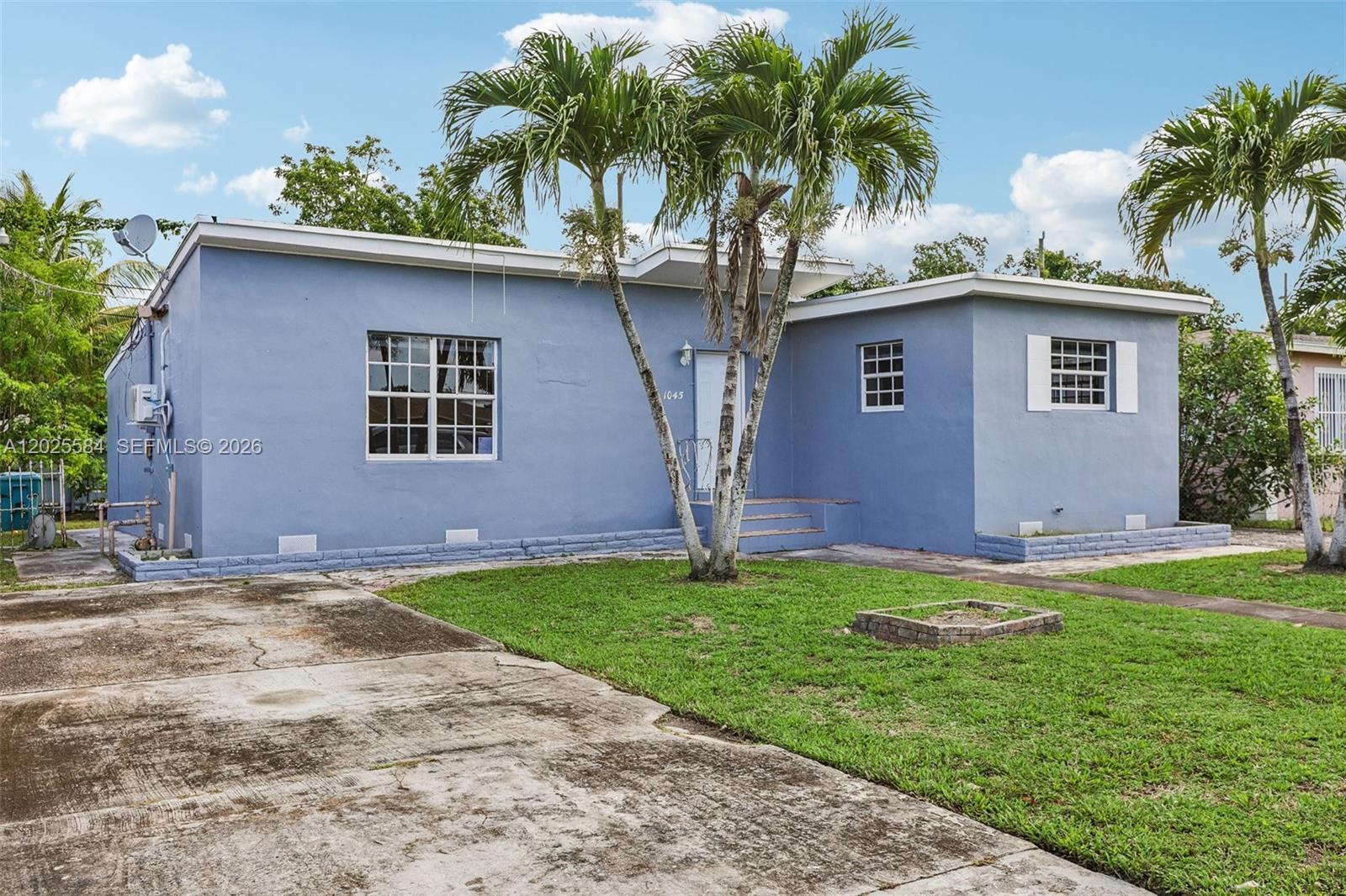 A blue single-story house features a front walkway, two palm trees, and a grassy lawn — 1045 NW 115th St, Miami FL 33168, MIAMI, FL