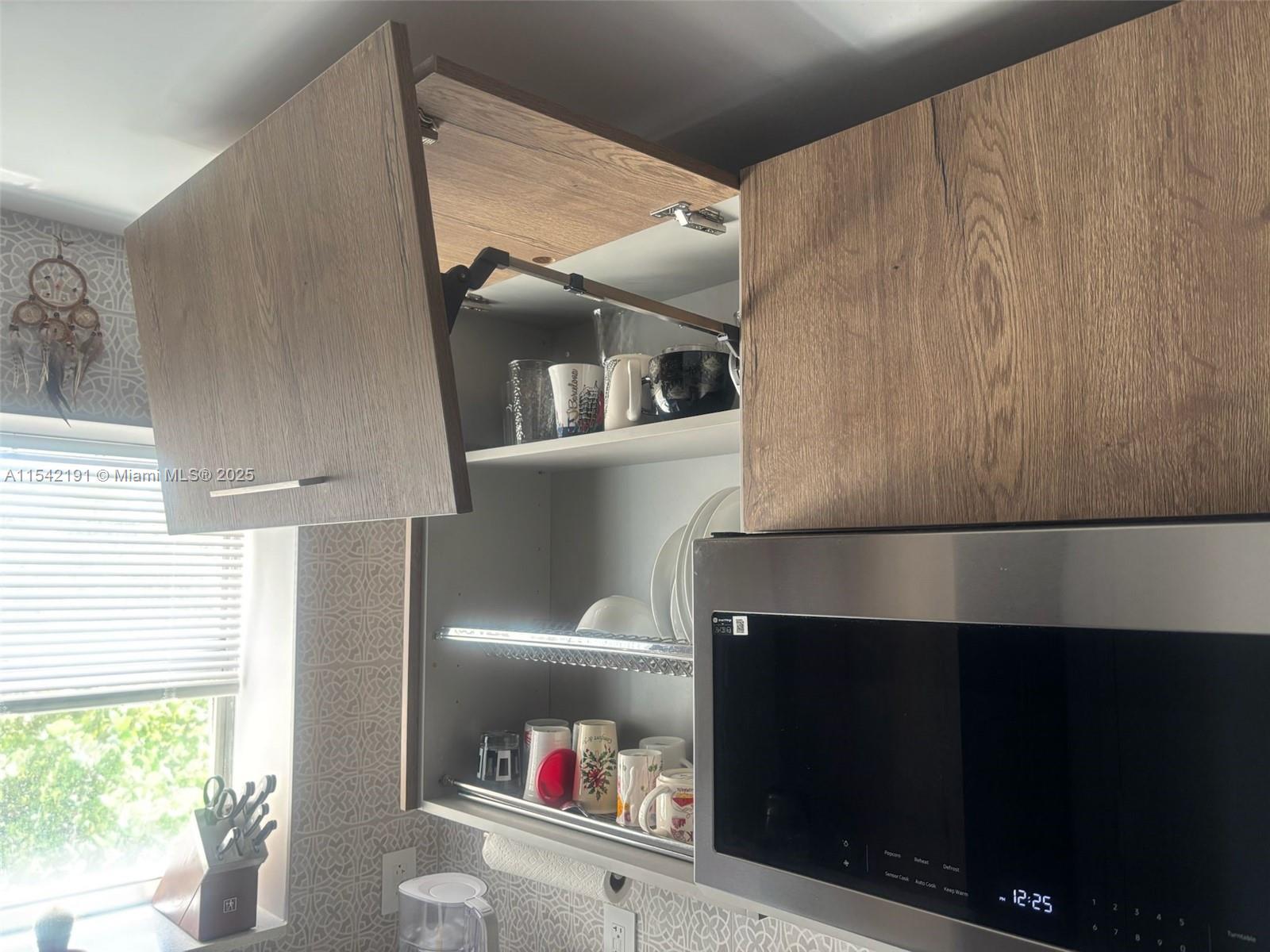 A kitchen cabinet with an open lift-up door reveals dishes above a stainless steel microwave — 1865 S Ocean Dr # 4F, Hallandale Beach FL 33009, HALLANDALE BEACH, FL