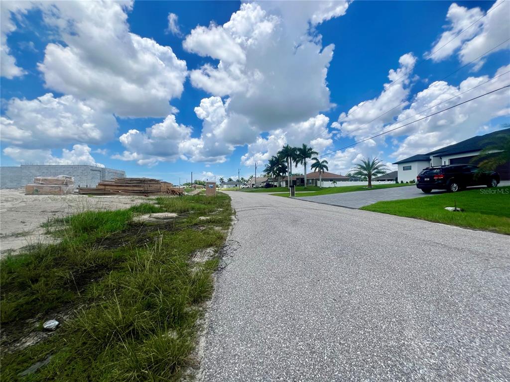 A paved street runs between a construction site with lumber and a residential house — 530 NW 18TH PLACE, CAPE CORAL, FL