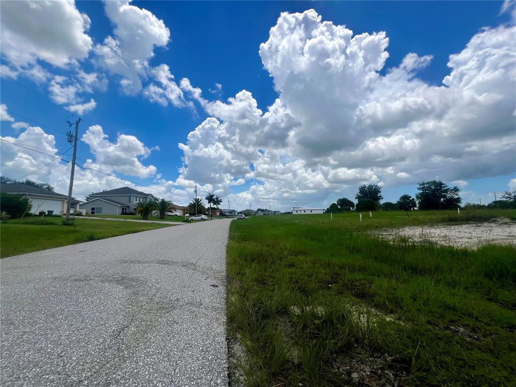 A paved road runs alongside a grassy vacant lot under a bright, cloudy blue sky — 530 NW 18TH PLACE, CAPE CORAL, FL