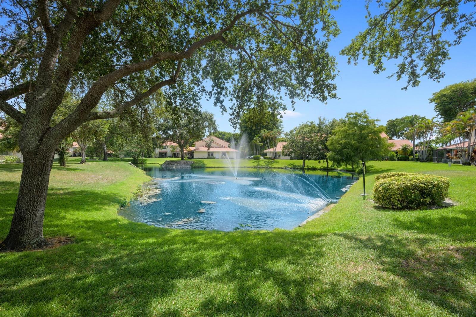 A pond with a fountain sits in a grassy yard surrounded by trees and houses — 6371 Boca Circle, Boca Raton FL 33433, BOCA RATON, FL