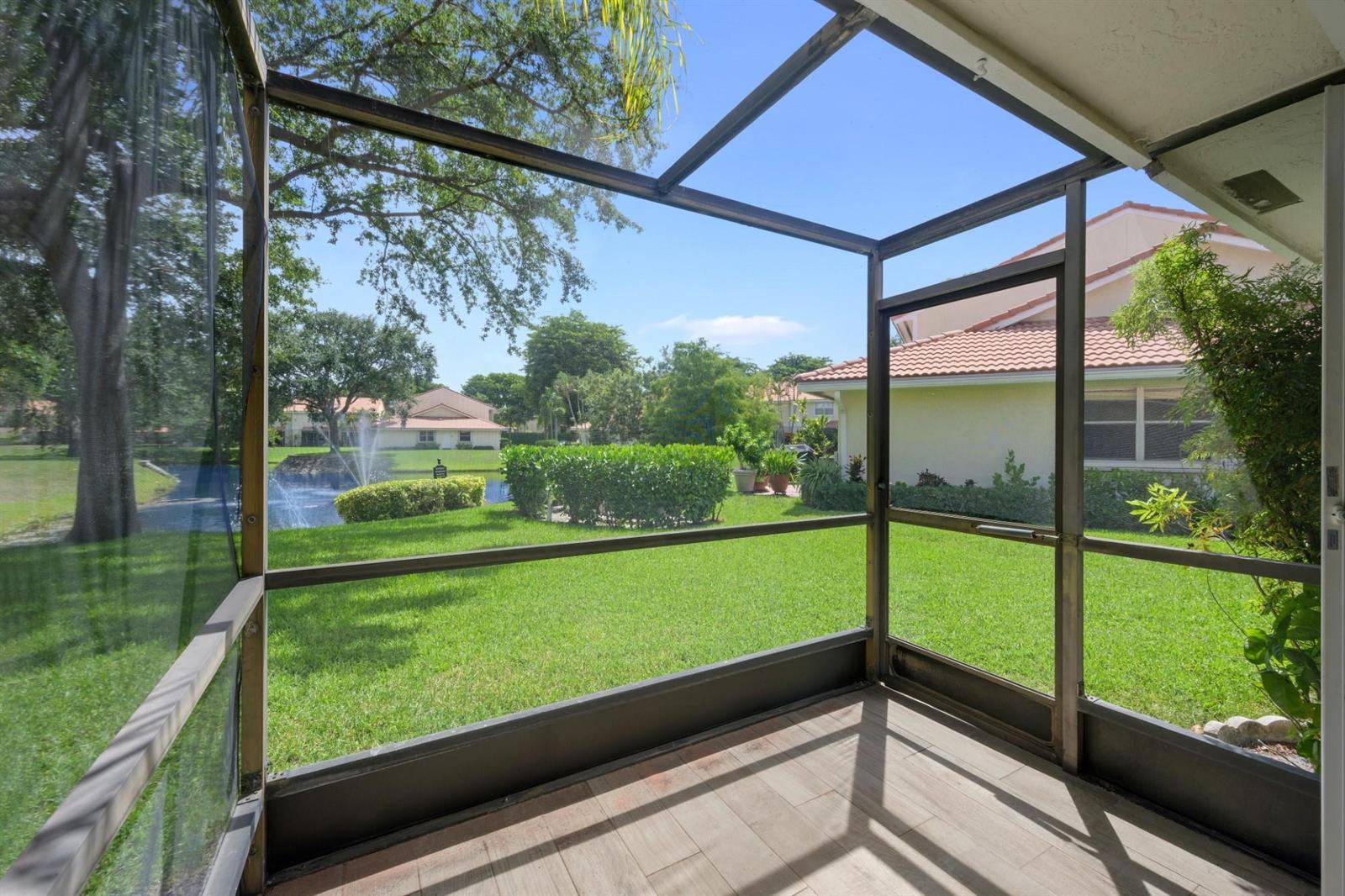 A screened-in patio with tile flooring overlooks a grassy backyard, a pond, and neighboring houses — 6371 Boca Circle, Boca Raton FL 33433, BOCA RATON, FL