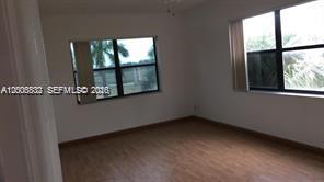 An empty room with light wood-look flooring and two windows overlooking outdoor greenery — 8290 LAKE DR # 412, Doral FL 33166, DORAL, FL