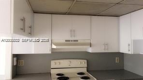 A kitchen features white cabinets, a light-colored range hood, and a white electric stove — 8290 LAKE DR # 412, Doral FL 33166, DORAL, FL