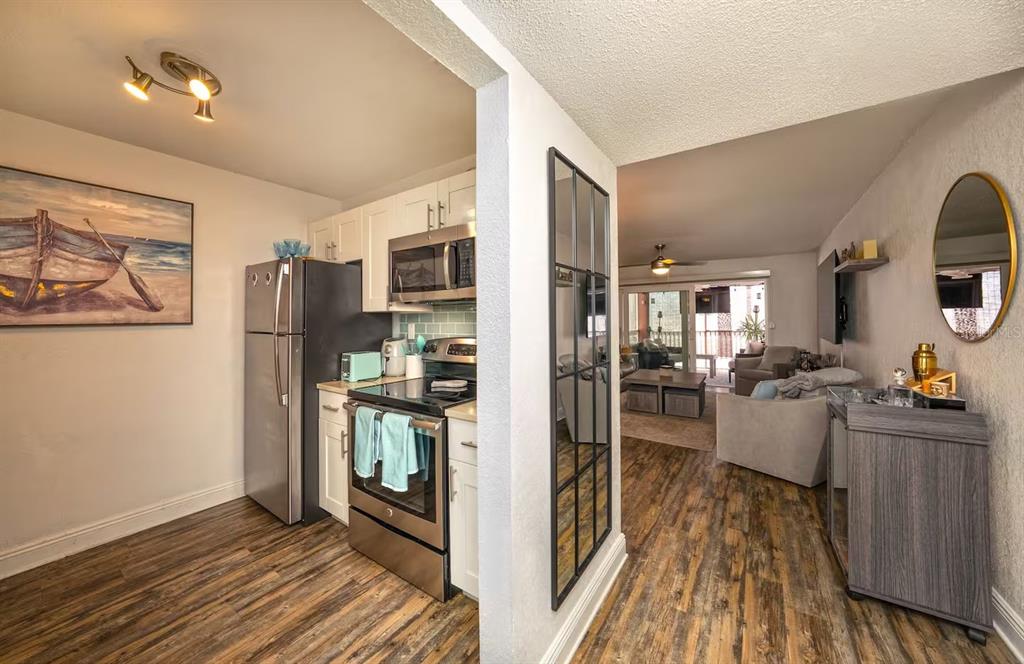 A kitchen with stainless steel appliances opens into a living room with wood-look flooring — 17035 GULF BOULEVARD UNIT 216, ST PETERSBURG, FL