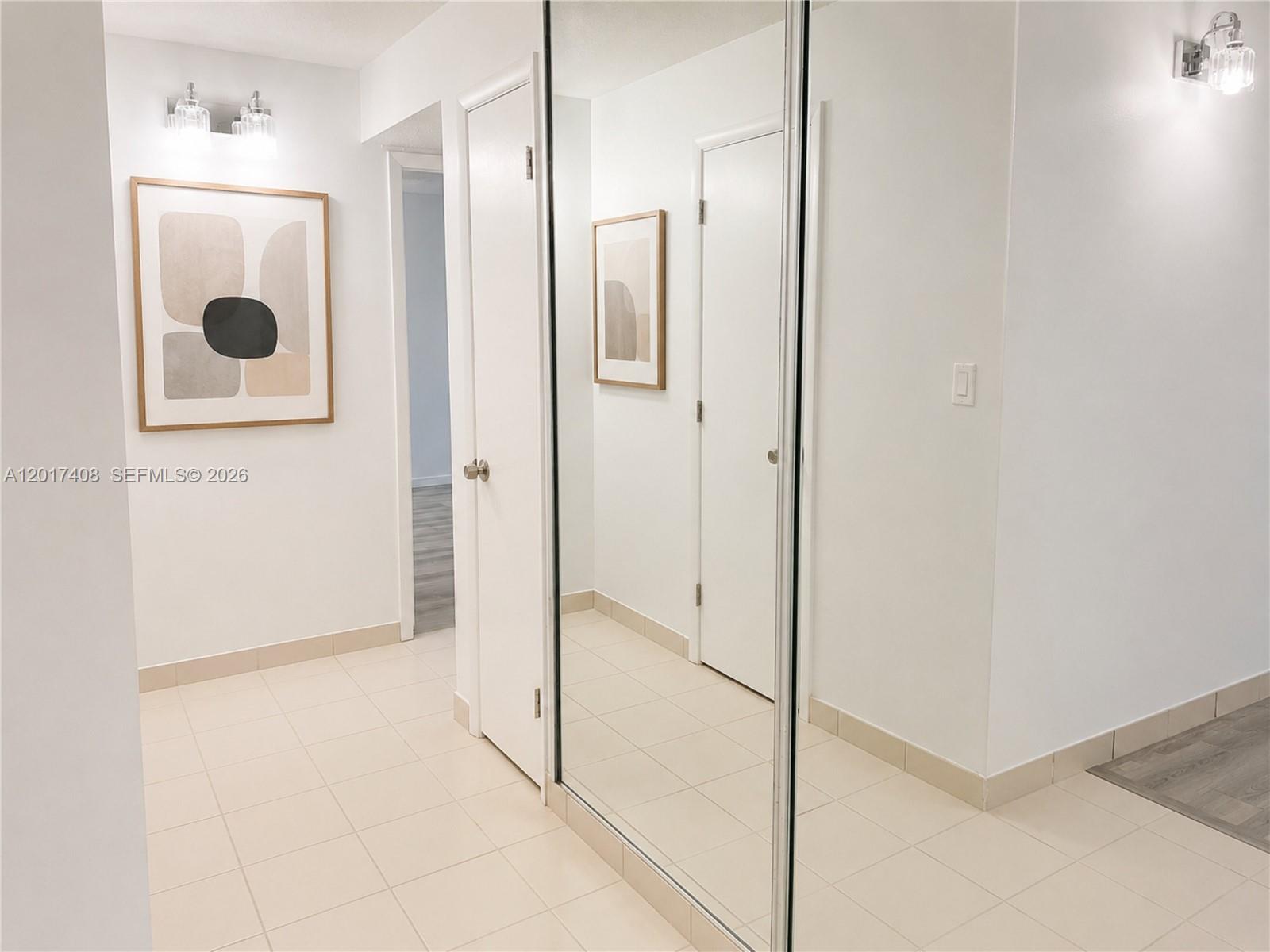 A bright hallway features light tile flooring, mirrored closet doors, and minimalist wall art — 14830 Naranja Lakes Blvd, Miami FL 33032, MIAMI, FL