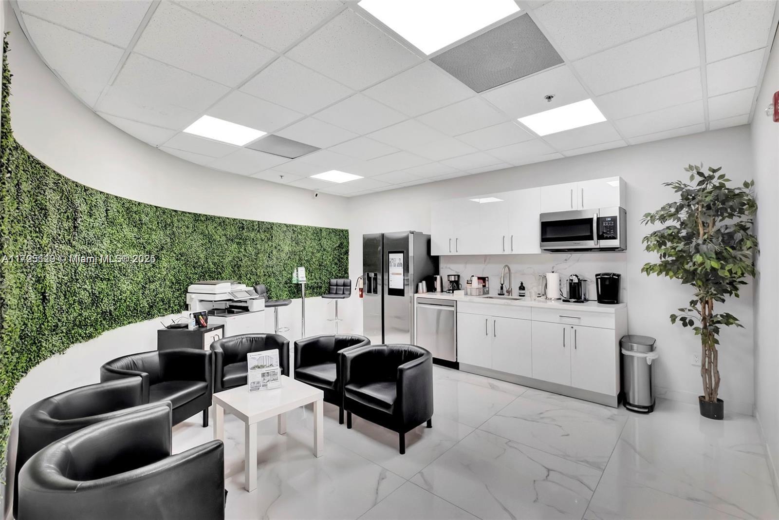 A modern office breakroom features white cabinetry, black leather chairs, and a green wall accent — 12550 Biscayne Blvd # 4, North Miami FL 33181, NORTH MIAMI, FL