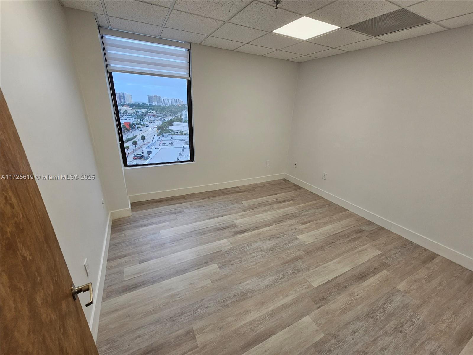 An empty office features light wood-look flooring, white walls, and a window with city views — 12550 Biscayne Blvd # 4, North Miami FL 33181, NORTH MIAMI, FL