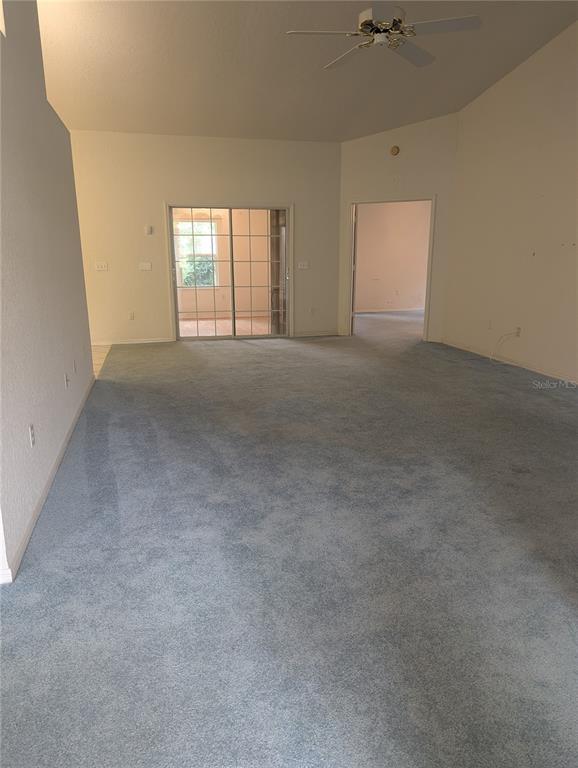 A spacious living room features blue carpeting, a vaulted ceiling with a fan, and sliding doors — 10816 SW 83RD AVENUE, OCALA, FL