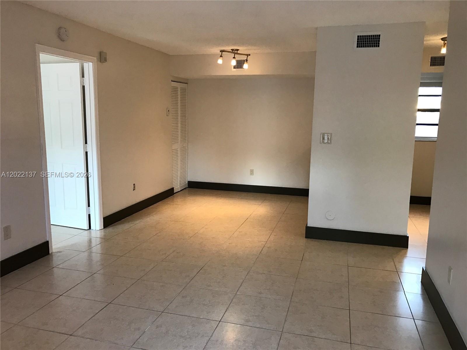 An empty room features beige tile flooring, white walls, dark baseboards, and a ceiling light fixture — 18224 Mediterranean Blvd # 17, Miami FL 33015, MIAMI, FL