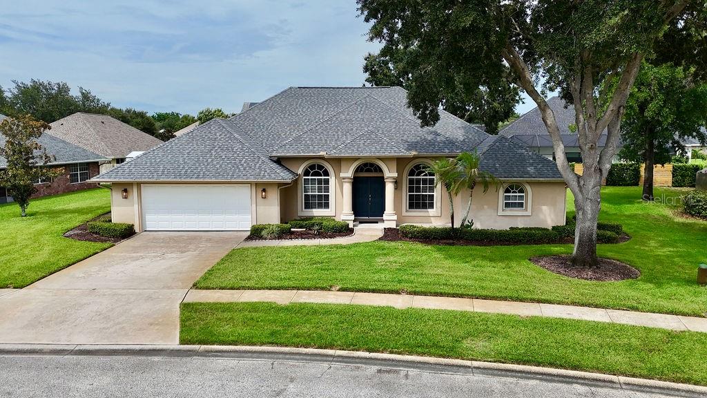 A single-story house with a gray shingled roof, beige stucco exterior, and a two-car garage — 1525 DATE DRIVE DRIVE, TITUSVILLE, FL