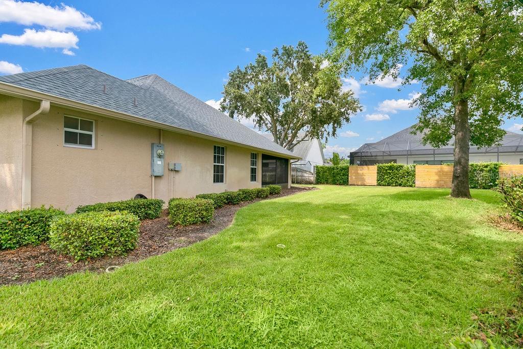 The exterior side of a beige house features a lawn, landscaping, and a large tree — 1525 DATE DRIVE DRIVE, TITUSVILLE, FL