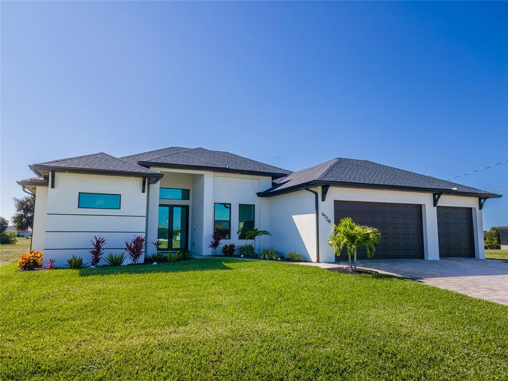 A modern single-story house with a white exterior, dark roof, and a three-car garage — 4126 NW 39TH STREET, CAPE CORAL, FL