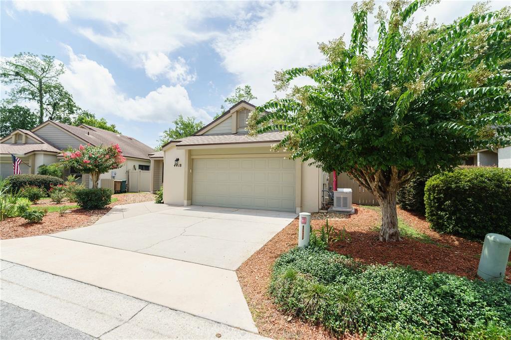 A single-story house with a beige garage, a concrete driveway, and a large flowering tree — 4418 NE 4TH STREET, OCALA, FL