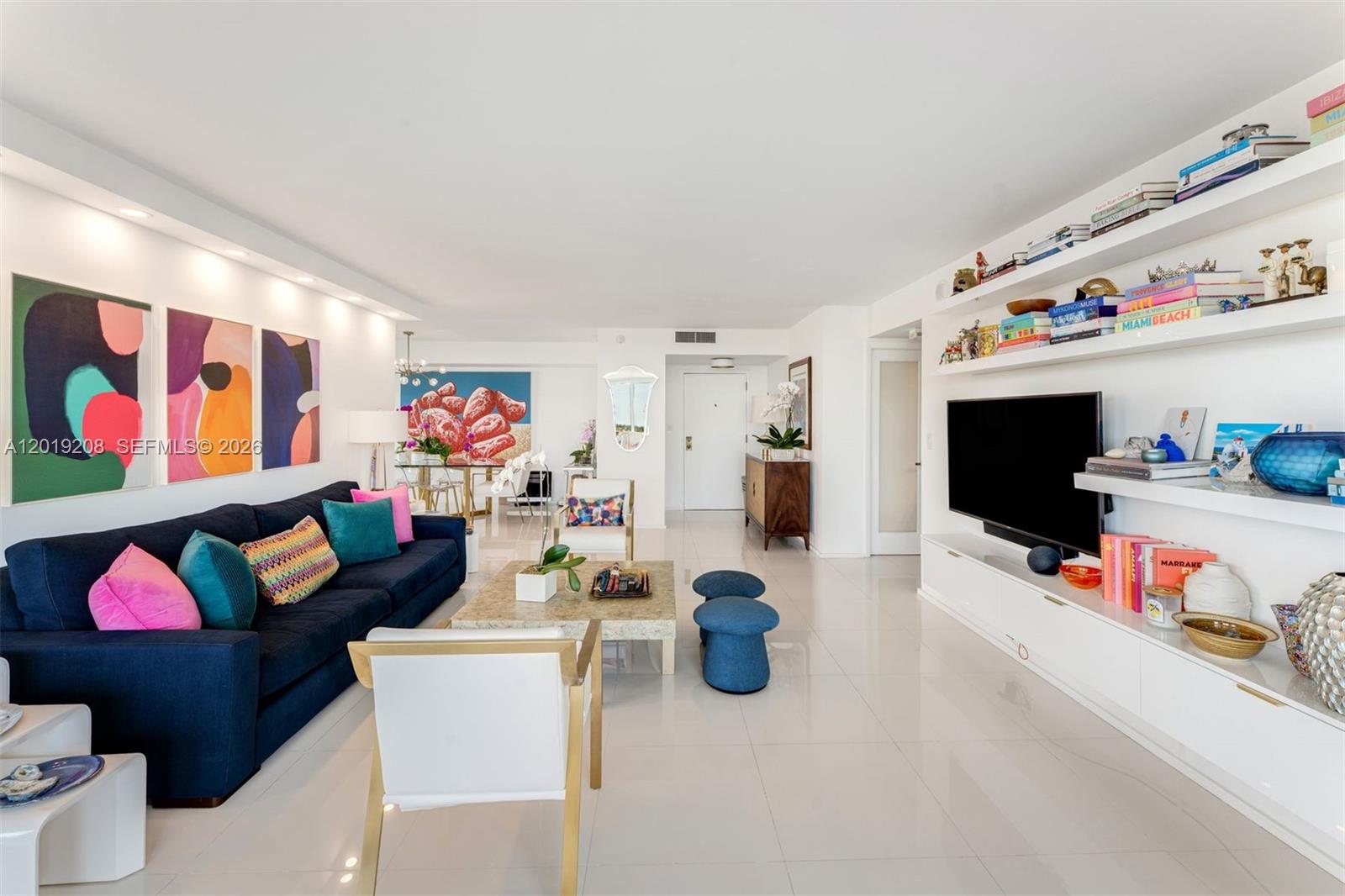 A bright living room features a dark blue sofa, white shelving, and colorful wall art — 1000 Quayside Ter # 901, Miami FL 33138, MIAMI, FL