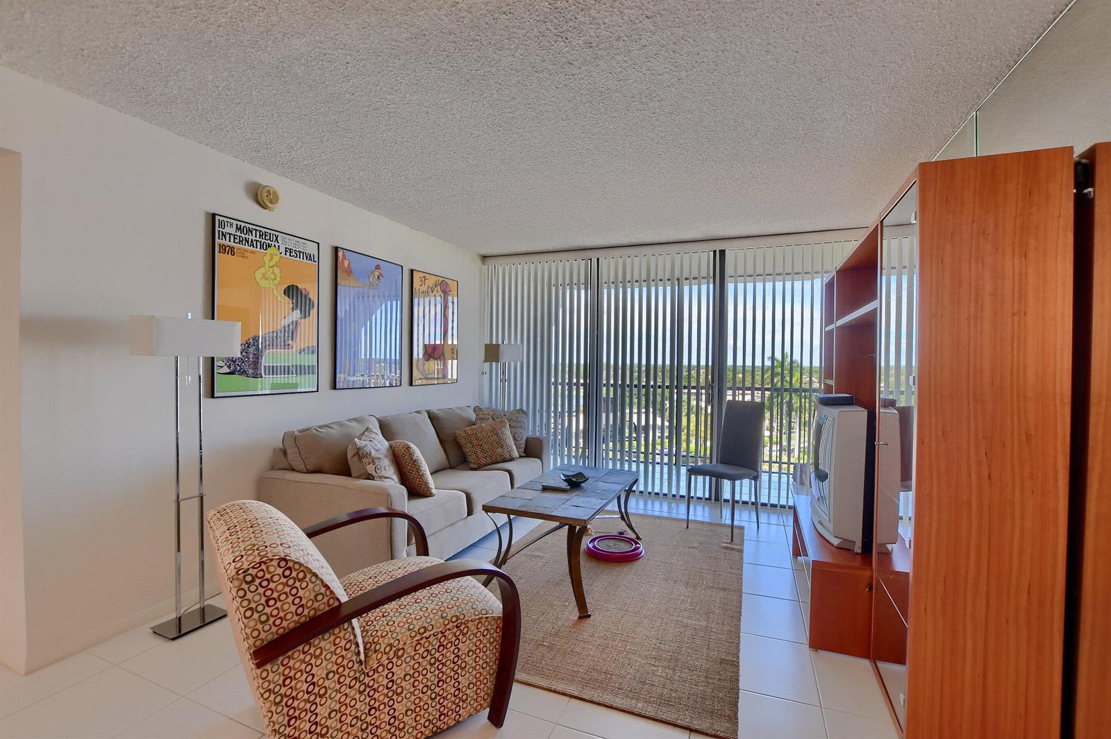 A living room features a beige sofa, patterned armchair, coffee table, and floor-to-ceiling window blinds — 7754 Lakeside Boulevard # 483, Boca Raton FL 33434, BOCA RATON, FL