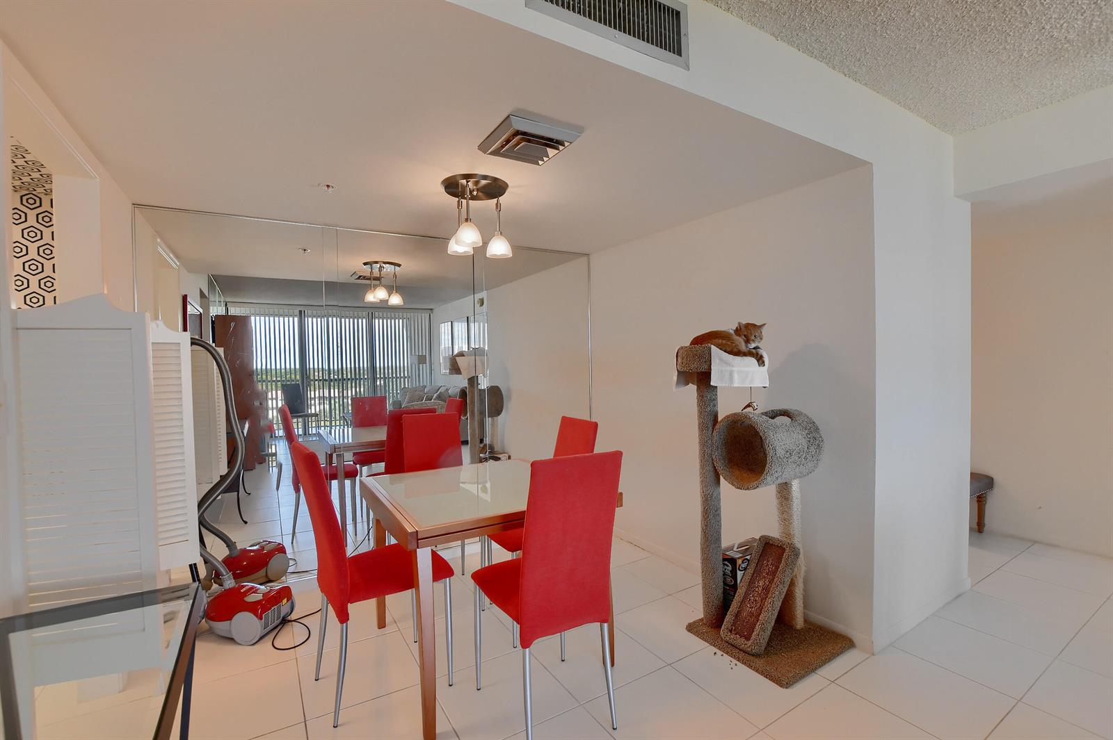 A dining area features a glass-top table, four red chairs, a mirrored wall, and a cat tree — 7754 Lakeside Boulevard # 483, Boca Raton FL 33434, BOCA RATON, FL