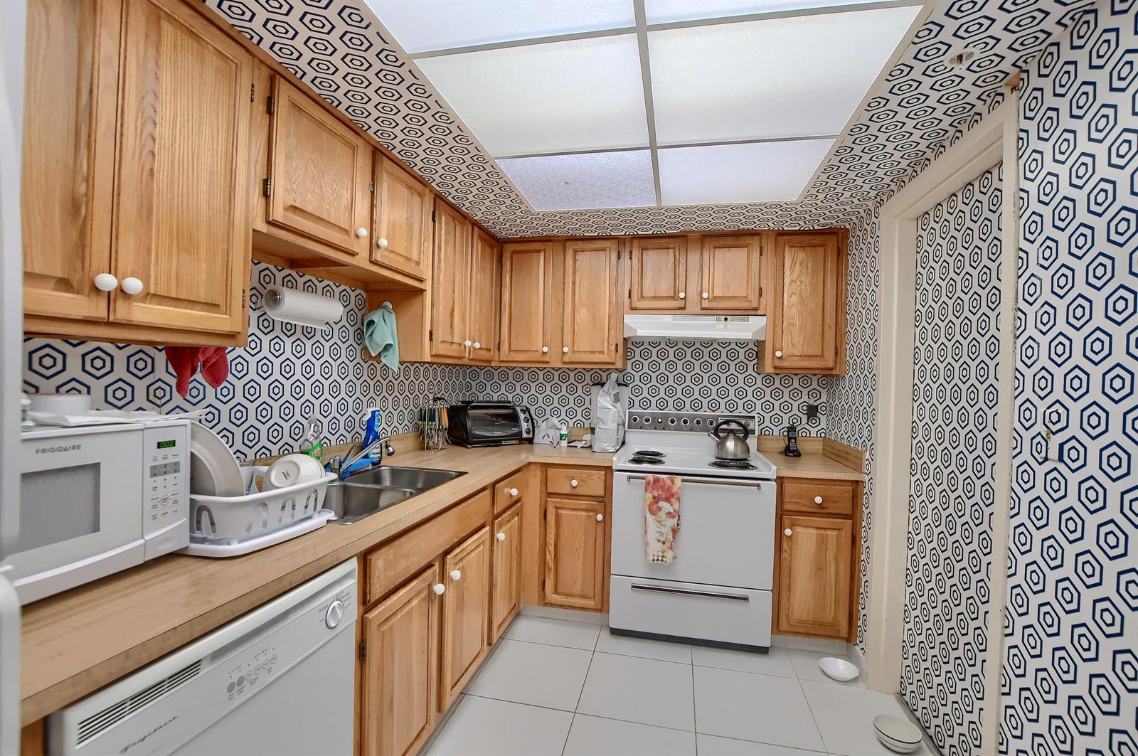 A kitchen with wood cabinets, white appliances, and walls covered in blue and white wallpaper — 7754 Lakeside Boulevard # 483, Boca Raton FL 33434, BOCA RATON, FL