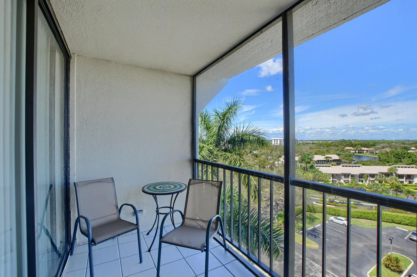 A screened-in balcony features two chairs, a small table, and a view of palm trees — 7754 Lakeside Boulevard # 483, Boca Raton FL 33434, BOCA RATON, FL