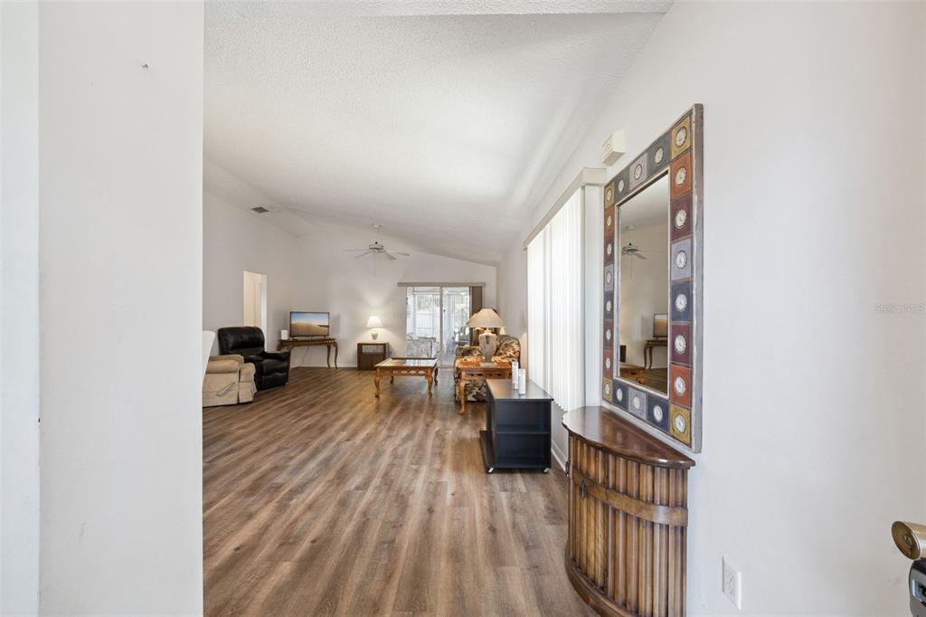 A living room with wood-look flooring, a vaulted ceiling, and a decorative wall mirror — 25312 GREEN HERON DRIVE, LEESBURG, FL