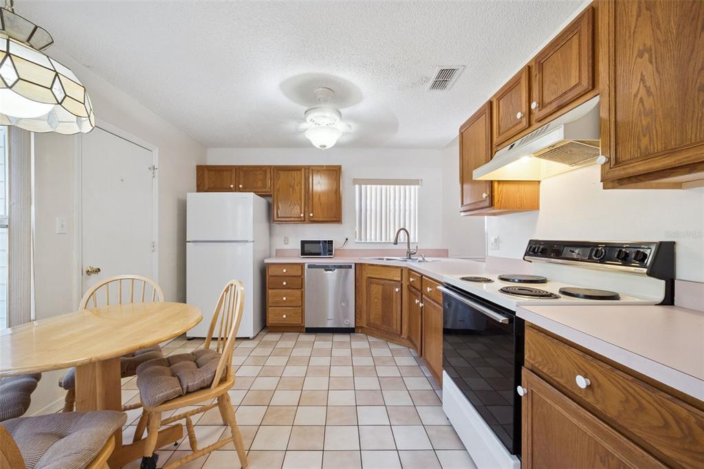 A kitchen with oak cabinets, white appliances, tile flooring, and a small dining table — 25312 GREEN HERON DRIVE, LEESBURG, FL