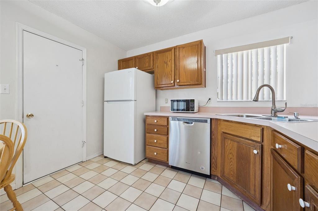 A kitchen features wood cabinets, a white refrigerator, a stainless steel dishwasher, and tile flooring — 25312 GREEN HERON DRIVE, LEESBURG, FL