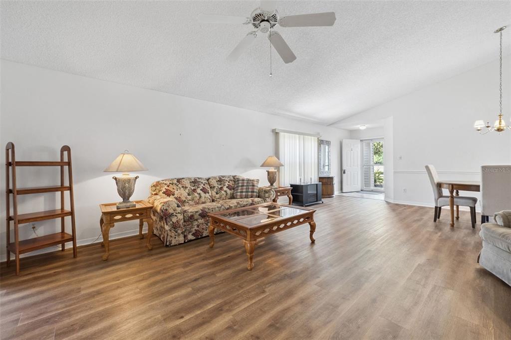 A living room features wood-look flooring, a floral sofa, a coffee table, and a ceiling fan — 25312 GREEN HERON DRIVE, LEESBURG, FL