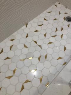 A close-up view of a shower floor featuring white hexagonal tiles with gold triangular accents — 392 Mansfield I, Boca Raton FL 33434, BOCA RATON, FL