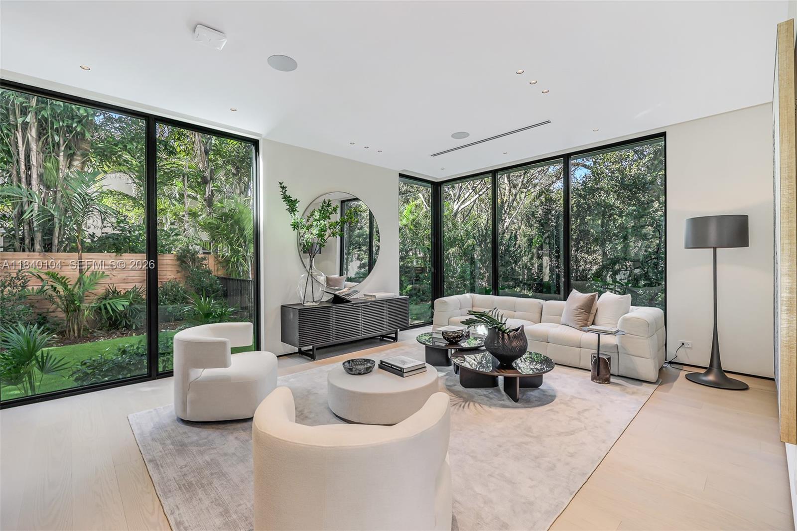 A modern living room features floor-to-ceiling windows, white furniture, and a view of lush greenery — 3860 Little Ave, Miami FL 33133, MIAMI, FL
