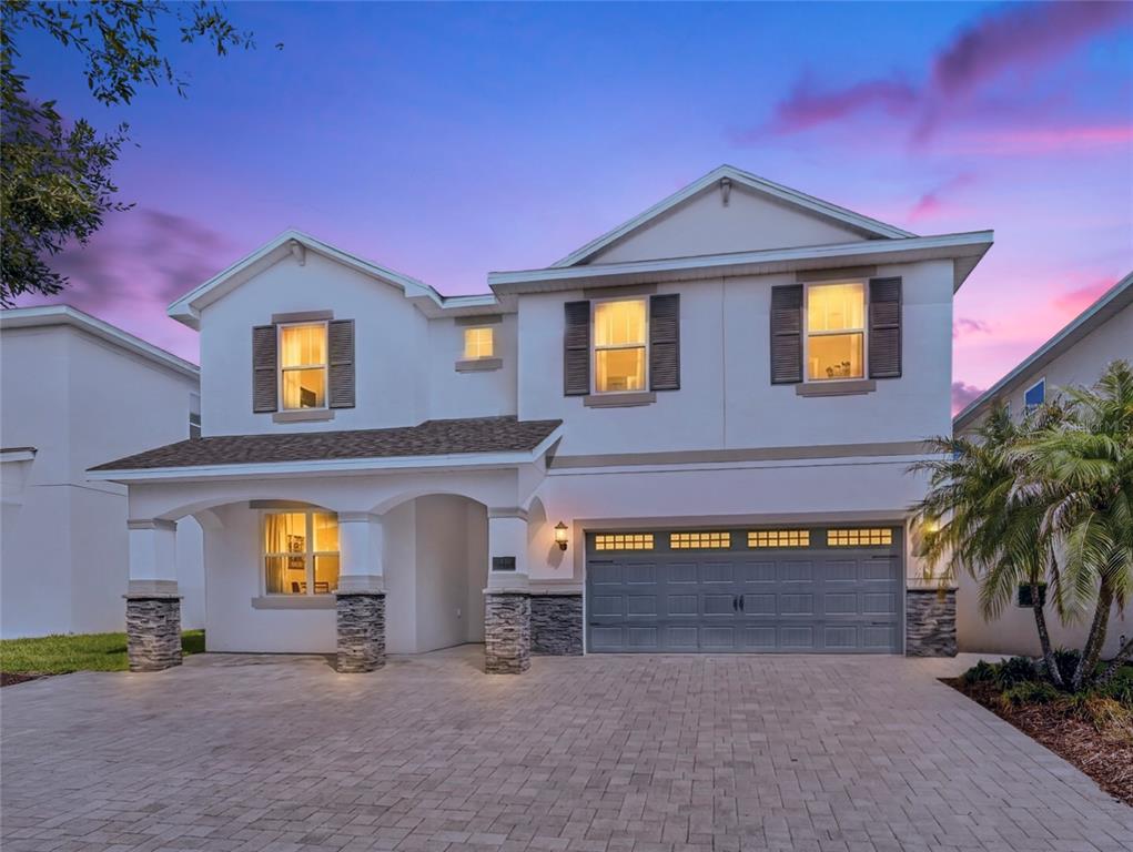 A two-story house with a white exterior, stone accents, and a paved driveway at dusk — 7450 MARKER AVENUE, KISSIMMEE, FL