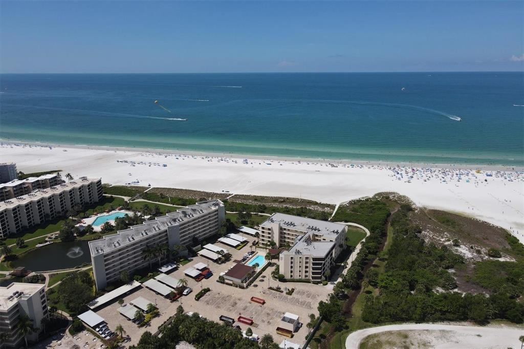 An aerial view shows beachfront condominiums with swimming pools and parking lots near the ocean — 5740 MIDNIGHT PASS ROAD UNIT 303F, SARASOTA, FL