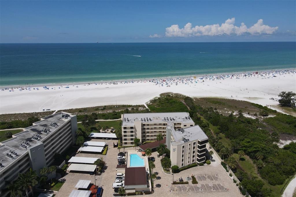 An aerial view shows two multi-story apartment buildings with a pool near a sandy beach — 5740 MIDNIGHT PASS ROAD UNIT 303F, SARASOTA, FL